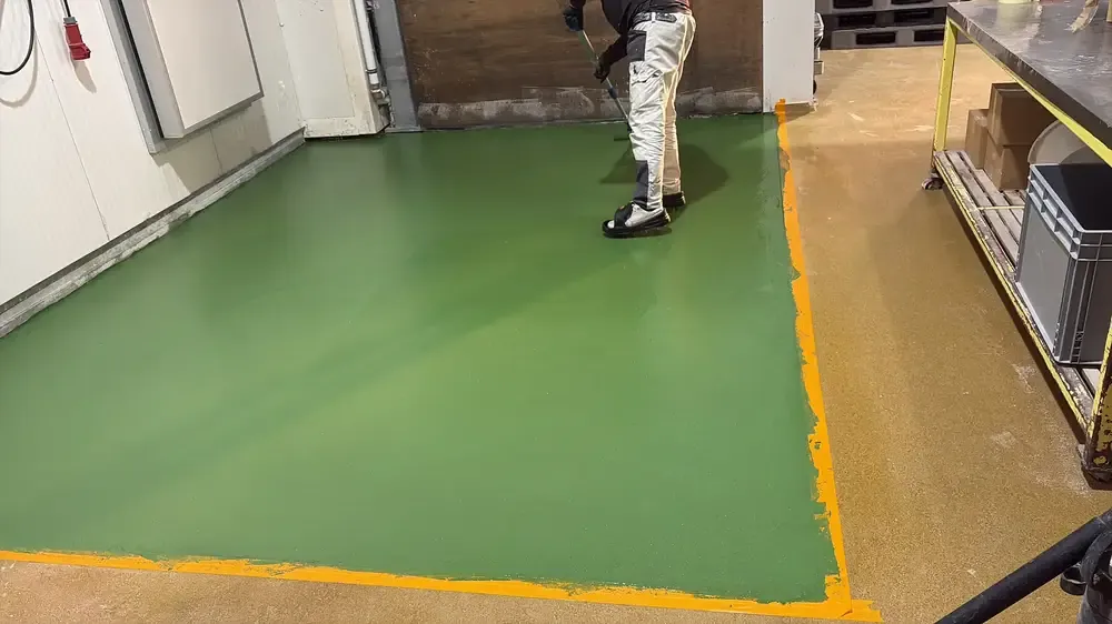 Sol vert en résine terminé, bordé de liserés orange, dans un local aux murs en panneaux blancs