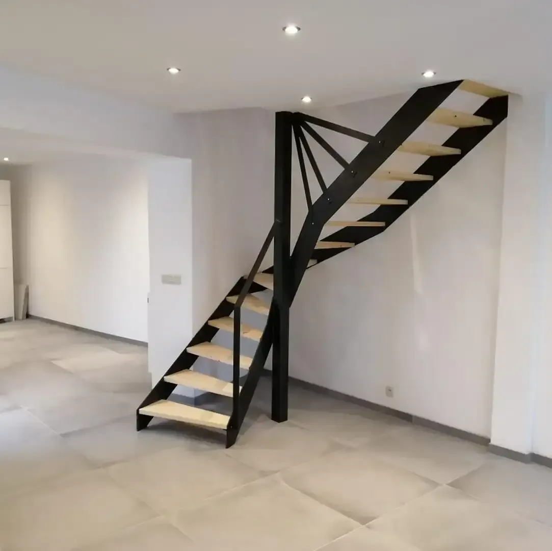 Escalier métallique noir à marches en bois clair, avec un quart tournant, dans un séjour aux murs blancs et au sol carrelé gris