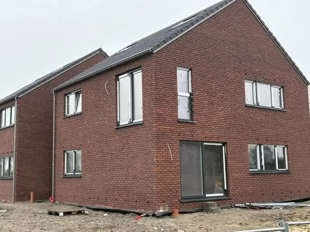 Deux maisons neuves en briques rouge foncé avec toit en ardoise et châssis posés, sur un terrain de chantier