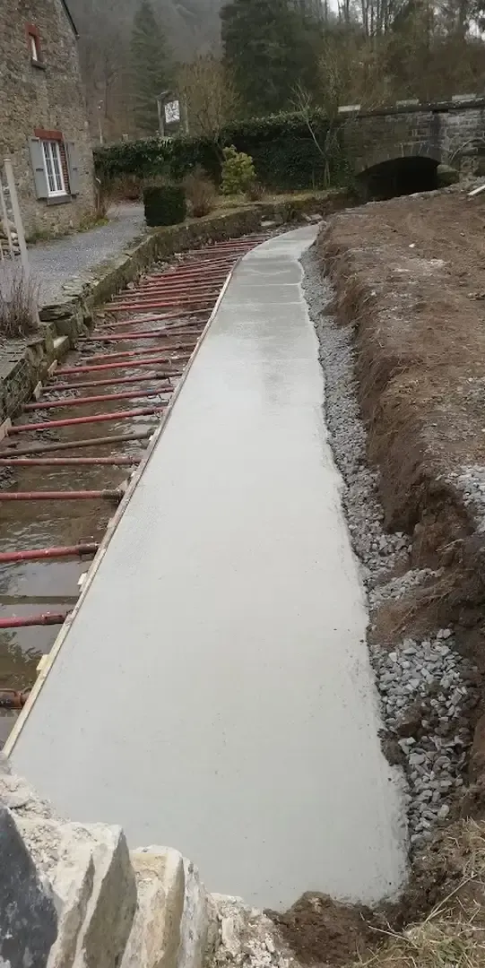 Dalle de béton lissée entre deux coffrages, le long d'un chemin et d'un mur de pierre