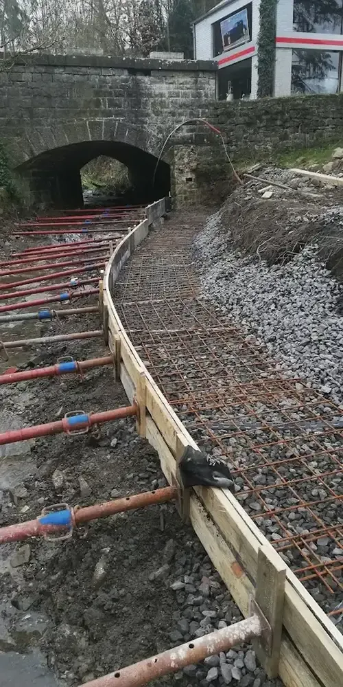 Coffrage en bois et armature d'acier d'un chemin de béton en courbe, pont voûté en pierre au fond