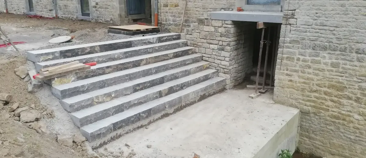 Escalier extérieur en pierre calcaire devant un mur en pierres, chantier en cours