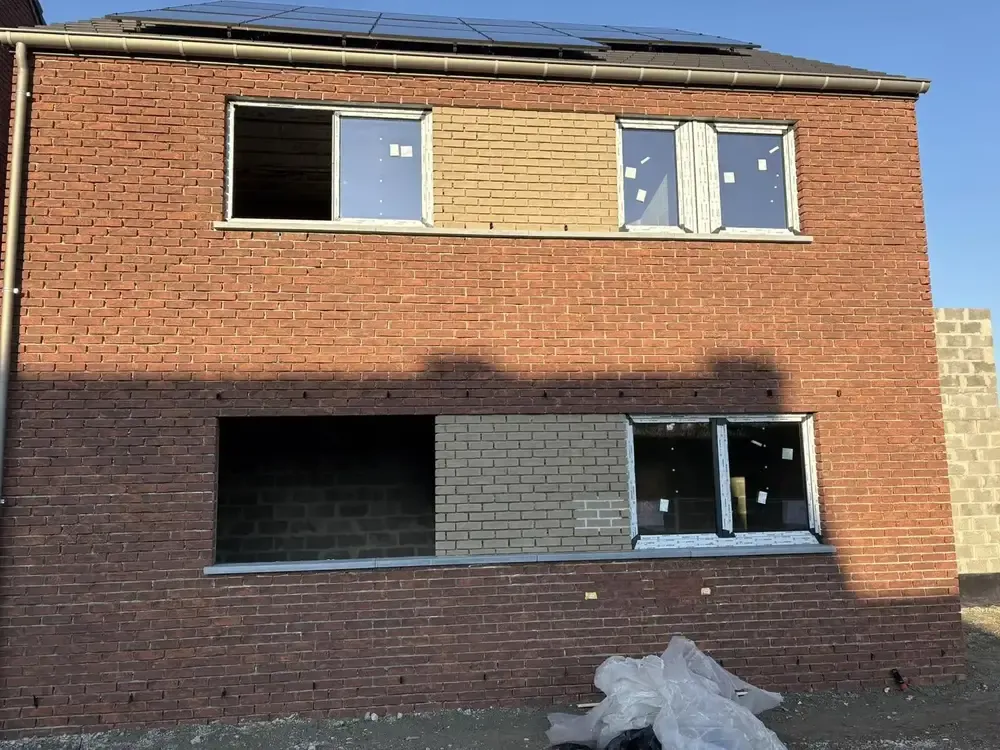 Façade en briques avec châssis posés au premier étage et ouvertures encore vides, panneaux solaires sur le toit