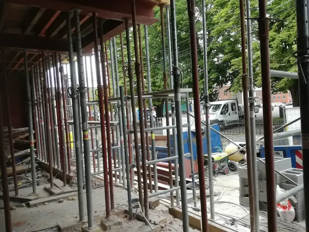 Vue de l'intérieur d'un percement de baie : poutres en bois soutenues par des étais métalliques, camionnette dans la rue