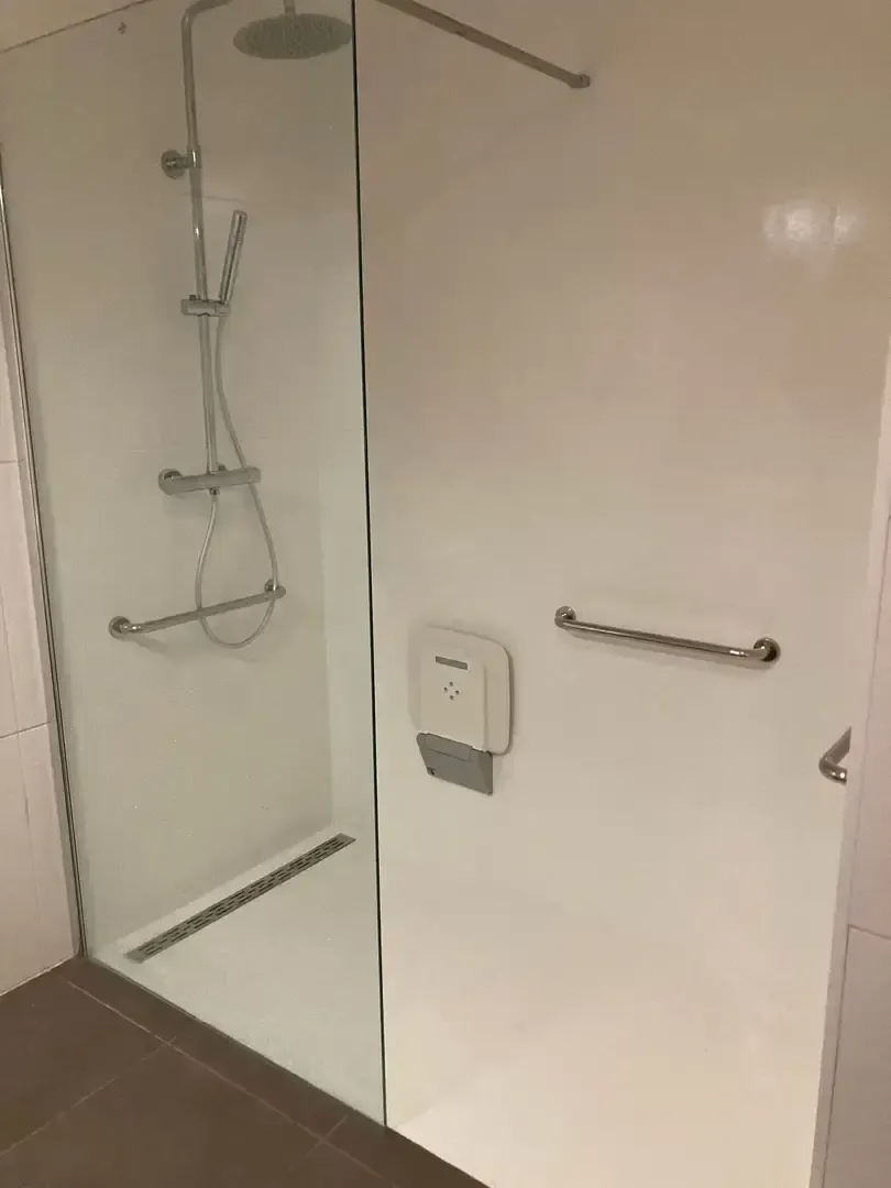 Douche à l'italienne avec paroi en verre, barres d'appui et caniveau, murs blancs et sol sombre