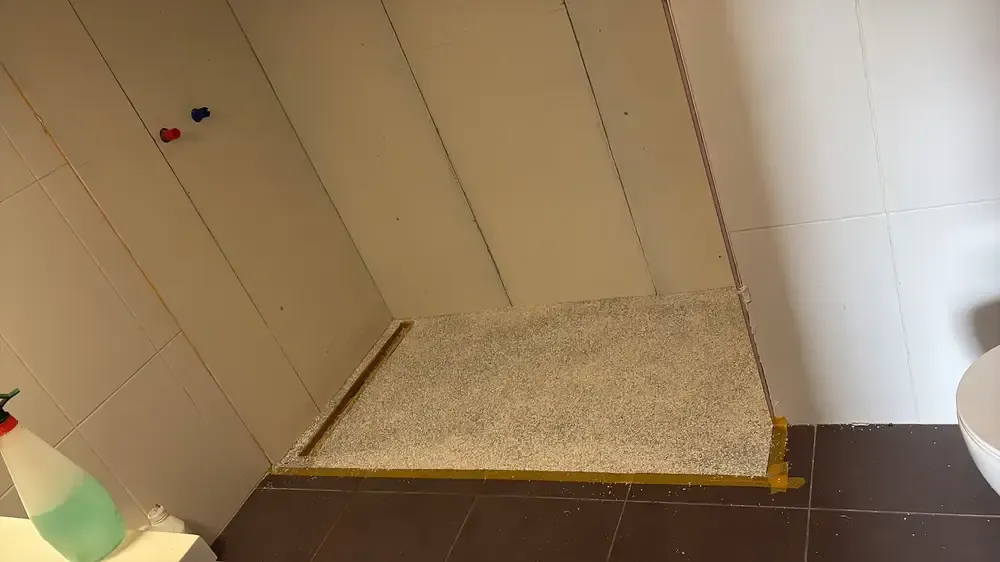 Receveur de douche en gravier clair délimité par des bandes de masquage, murs carrelés en blanc